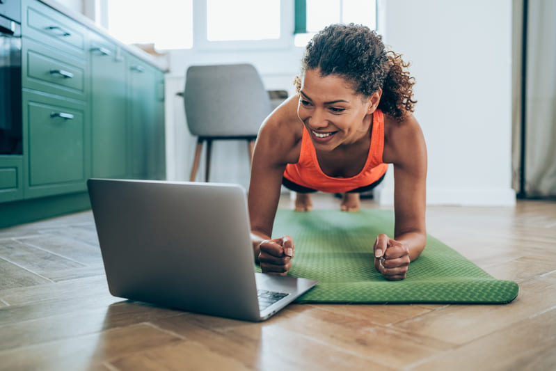 online-live-kurse Eine Frau macht eine Unterarmstütze auf einer grünen Sportmatte vor einem Laptop