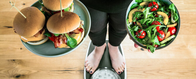 Person steht auf Waage mit Burger und Salat