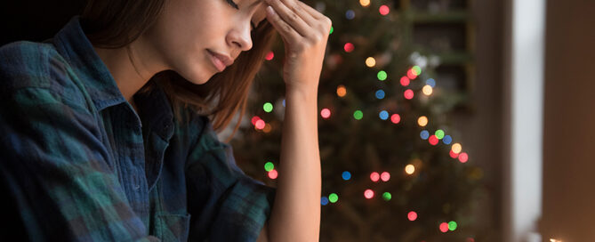 Frau mit Kopfschmerzen vor einem Weihnachtsbaum
