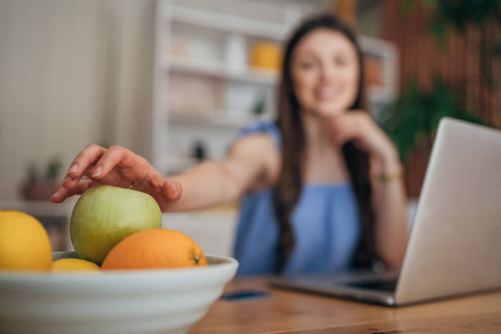 Frau greift in Obstschale Eine Frau greift in die Obstschale während sie arbeitet