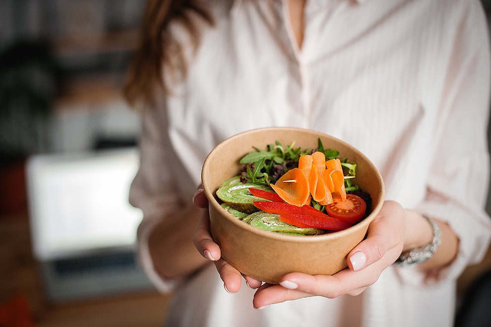Frau hält eine Schüssel mit Gemüse Gesunde Ernährung: Eine Frau hält eine Pappchale mit Salat und gesundem Essen.