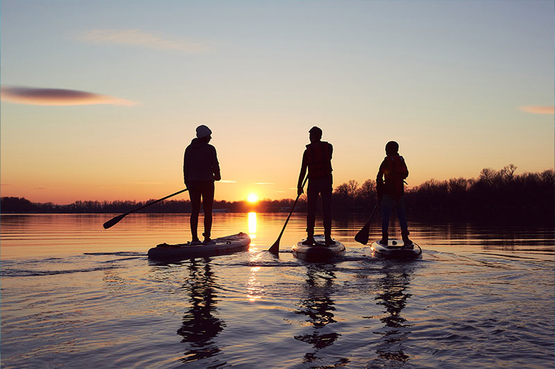 hansefit_firmenfitness_sportarten_04 Drei Personen fahren SUP im Sonnenuntergang