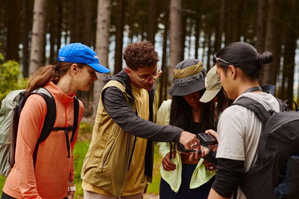 komoot-how-to-2 Das Bild zeigt 5 Personen im Walk in Wanderausstattung die zusammen auf ein Handy schauen.