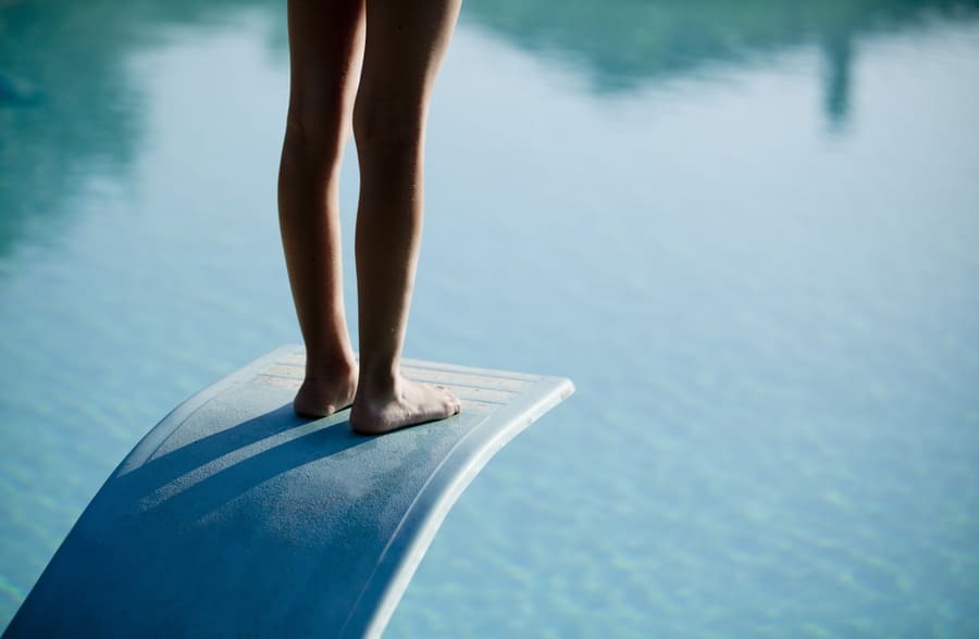 Eine Person steht auf einem Sprungbrett im Freibad.