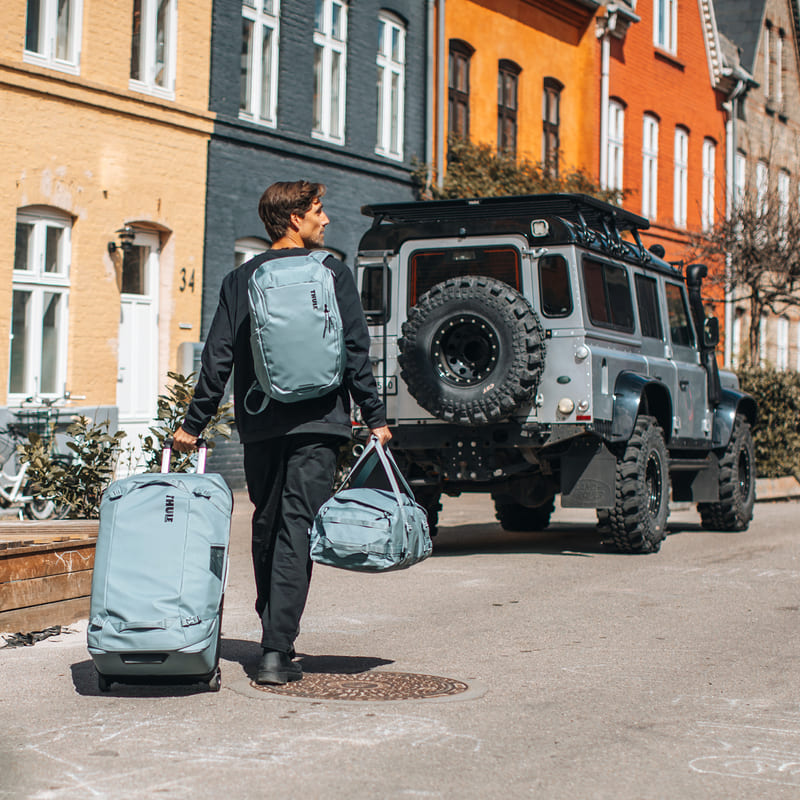 thule-artikelbild Ein Mann läuft durch eine Innenstadt und zieht einen Koffer hinter sich her.