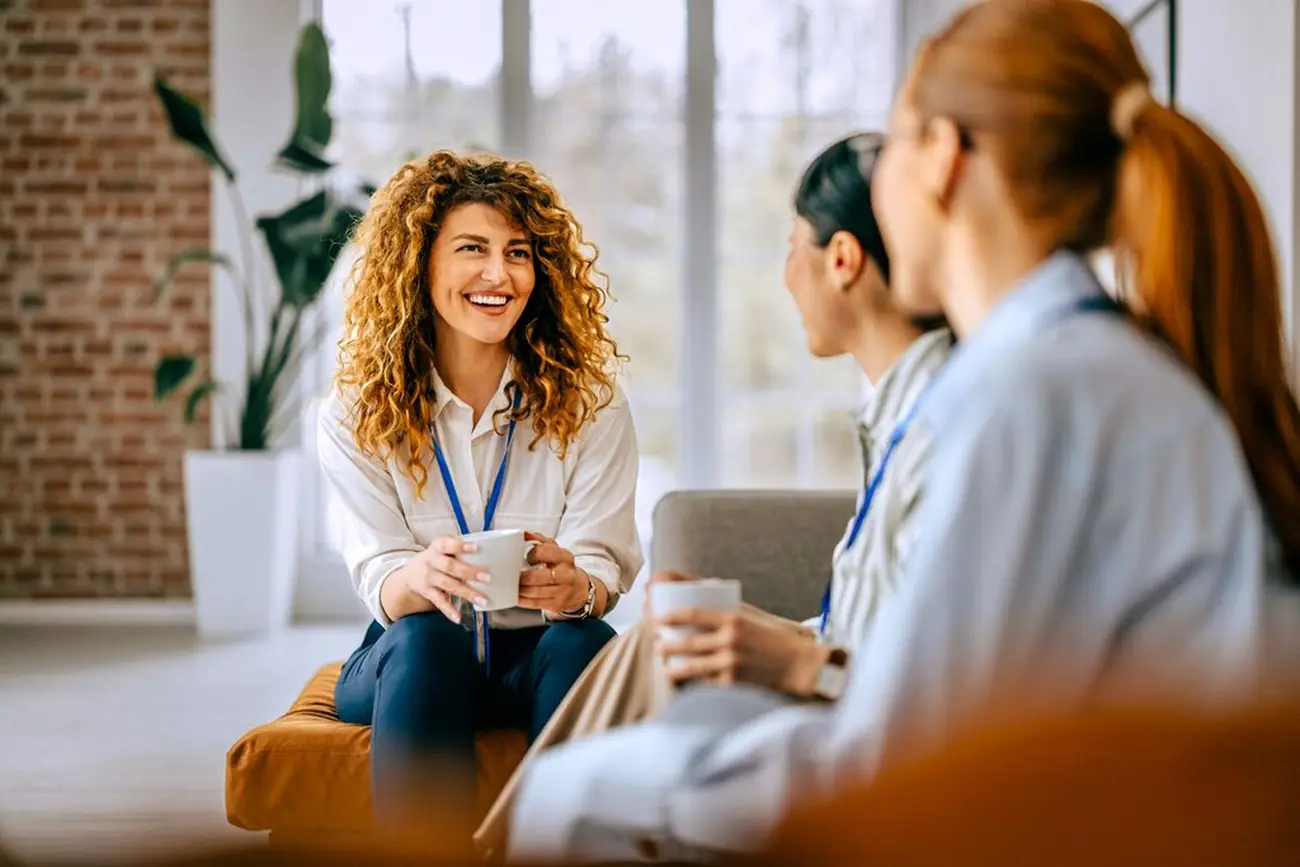Drei Mitarbeiterinnen unterhalten sich lachend beim Kaffeegespräch im Büro