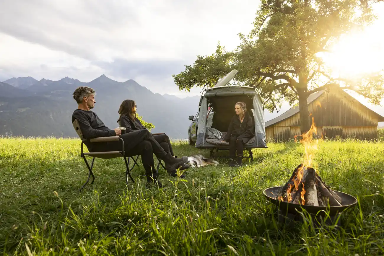 Gruppe entspannt sich beim Camping in den Bergen mit Thule-Ausrüstung und Lagerfeuer